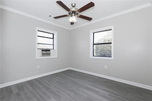 an empty room with wooden floor ceiling fan and windows
