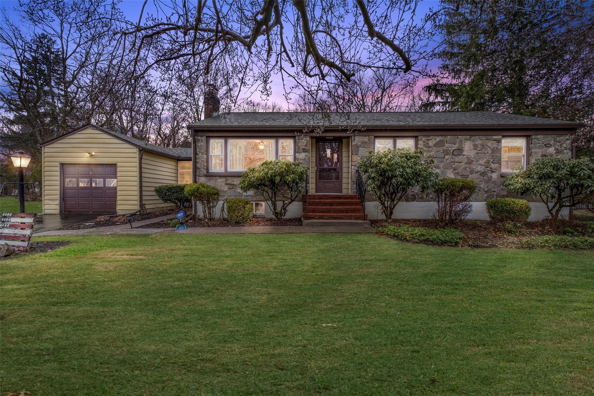 View of front of house with stone siding, a chimney, entry steps, and a lawn