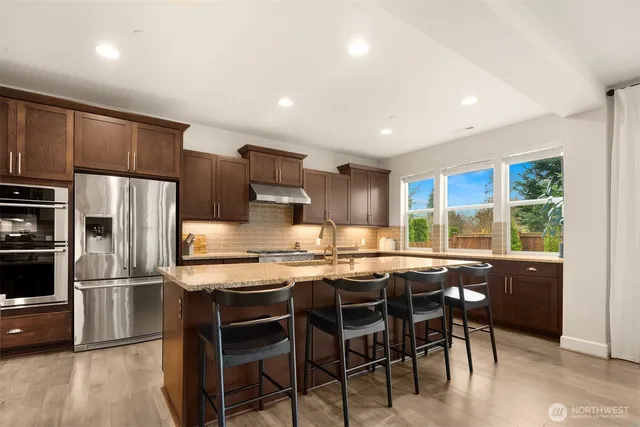 a kitchen with stainless steel appliances granite countertop a sink a stove and a wooden cabinets