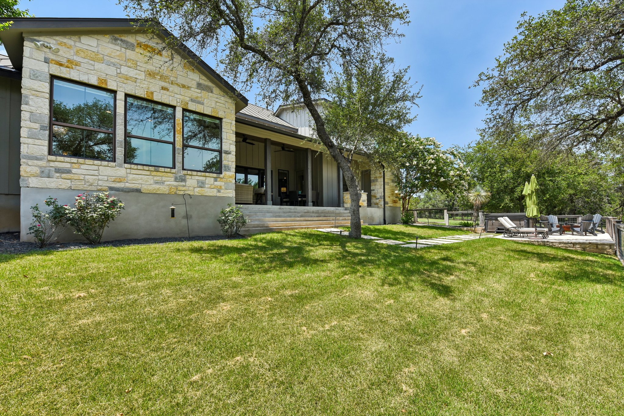 2203 Improver Road Spicewood, TX 78669 - Photo 28 of 38 A spacious lawn unfolds next to a stone-clad home featuring a deep covered patio and a tiered deck for outdoor leisure.