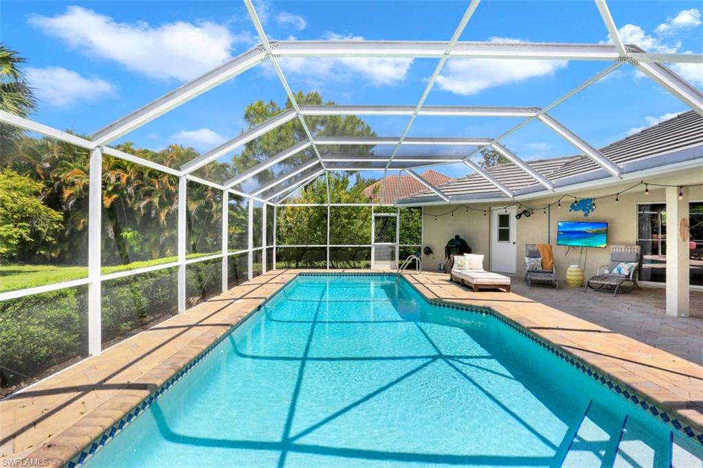 7359 Stonegate Drive Naples, FL 34109 - Photo 26 of 33 a view of a backyard with a large pool and a lawn chairs under an umbrella