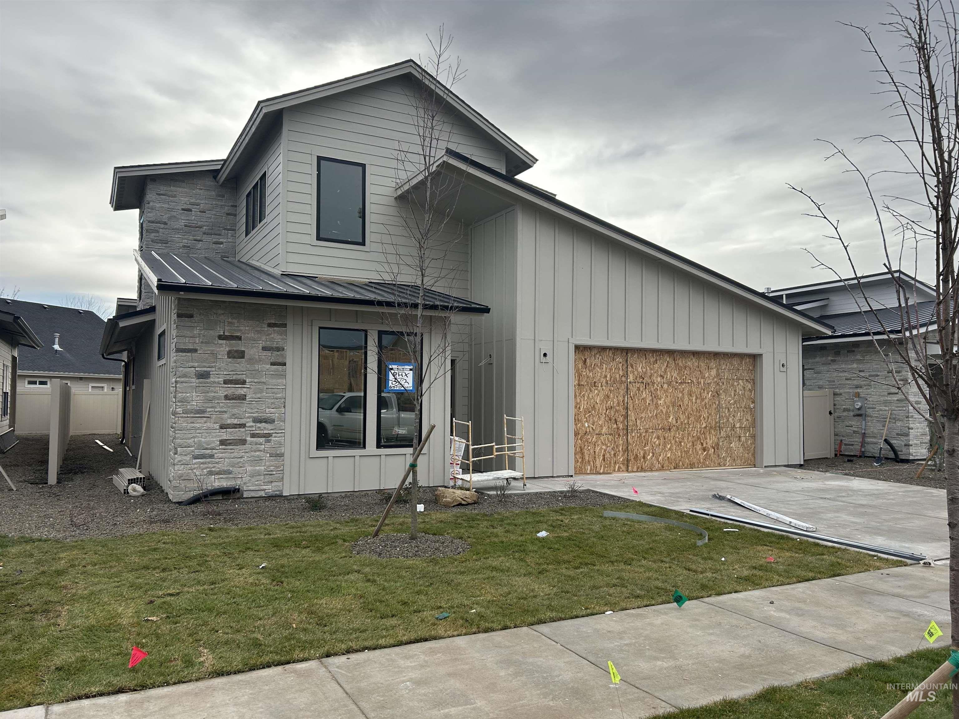 View of front of house with stone siding, board and batten siding, concrete driveway, a metal roof, and a garage