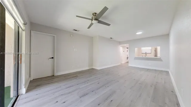 an empty room with wooden floor a ceiling fan and windows