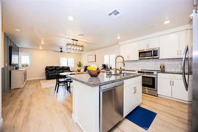 a kitchen with stainless steel appliances granite countertop a stove top oven a sink dishwasher a refrigerator and white cabinets with wooden floor