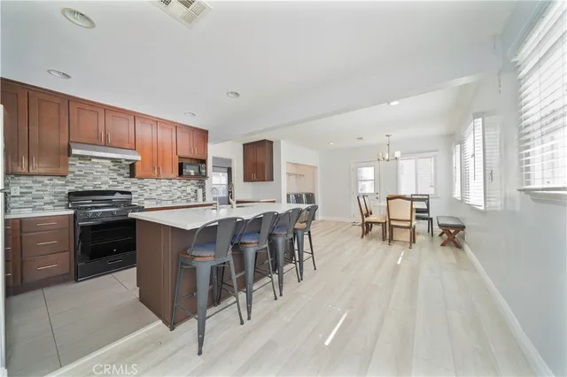 a open kitchen with stainless steel appliances granite countertop a stove a sink a dining table and chairs with wooden floor