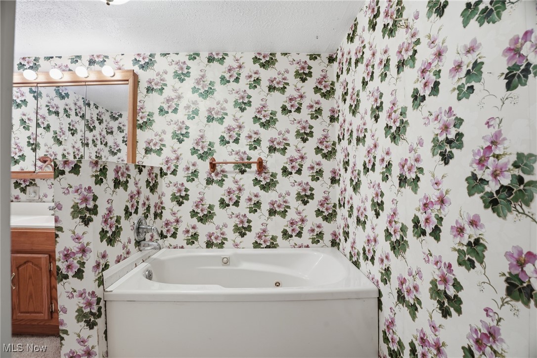 8045 Veto Road Belpre, OH 45714 - Photo 39 of 50 Bathroom featuring wallpapered walls, a tub with jets, a textured ceiling, and vanity