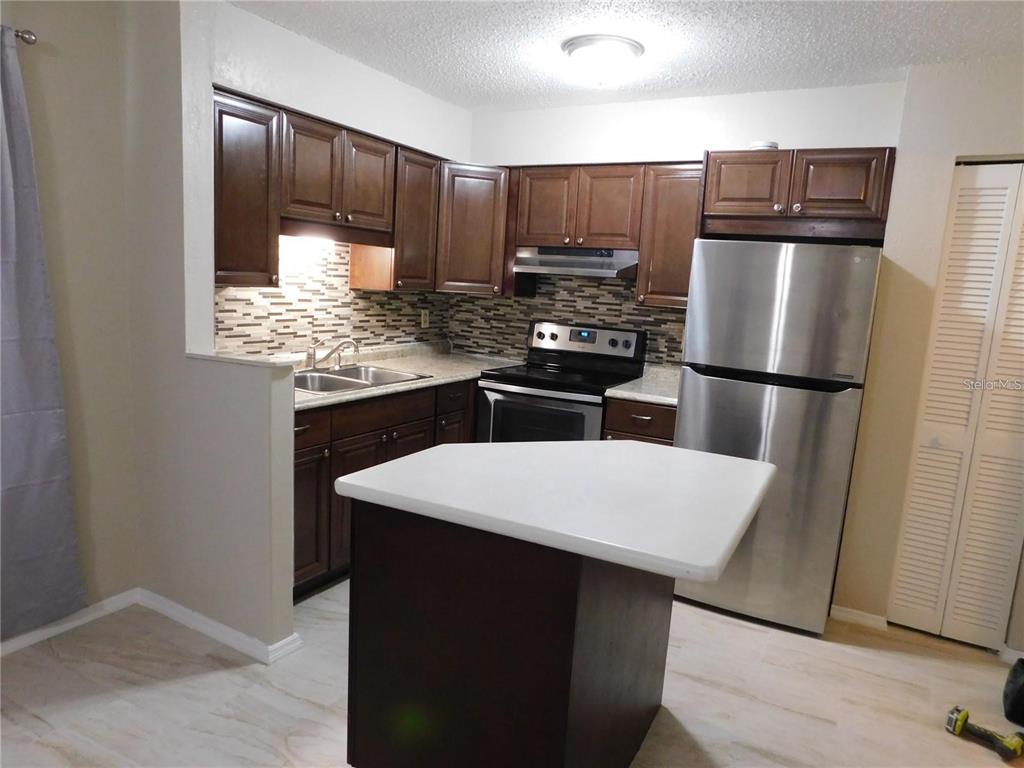 21150 Gertrude Avenue, Unit B4 Port Charlotte, FL 33952 - Photo 4 of 10 a kitchen with kitchen island granite countertop wooden cabinets and stainless steel appliances