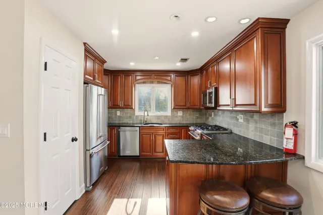 a kitchen with stainless steel appliances granite countertop a stove a sink dishwasher and a refrigerator with wooden floor