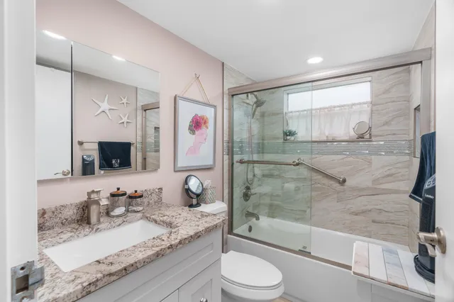 a bathroom with a granite countertop sink mirror vanity shower and toilet
