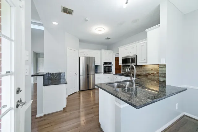 a kitchen with stainless steel appliances granite countertop a refrigerator a sink a stove and oven with wooden floor