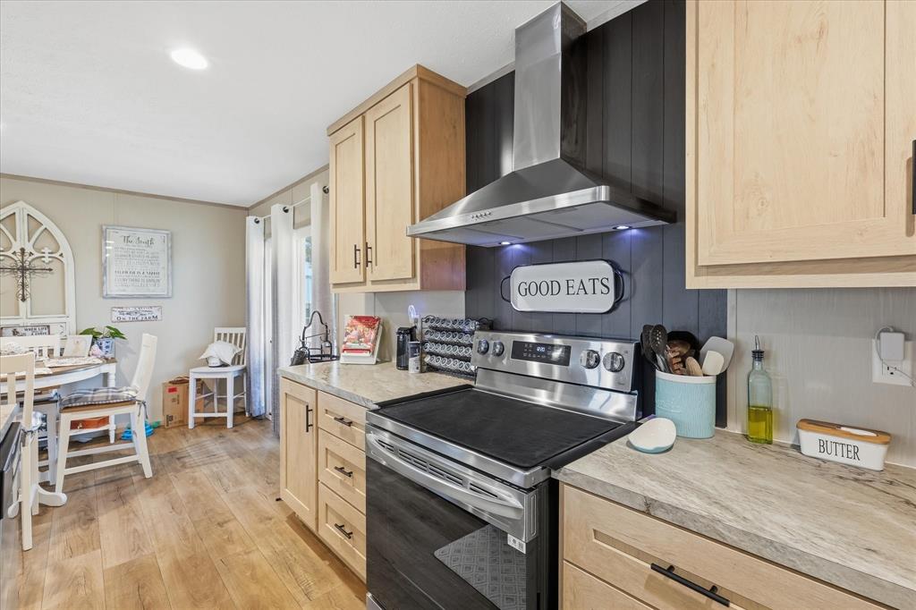 193 Firefly Drive Springtown, TX 76082 - Photo 11 of 32 Modern kitchen featuring stainless steel appliances, light wood-finish cabinetry, a black shiplap accent wall, light-toned countertops, and wood-finish flooring
