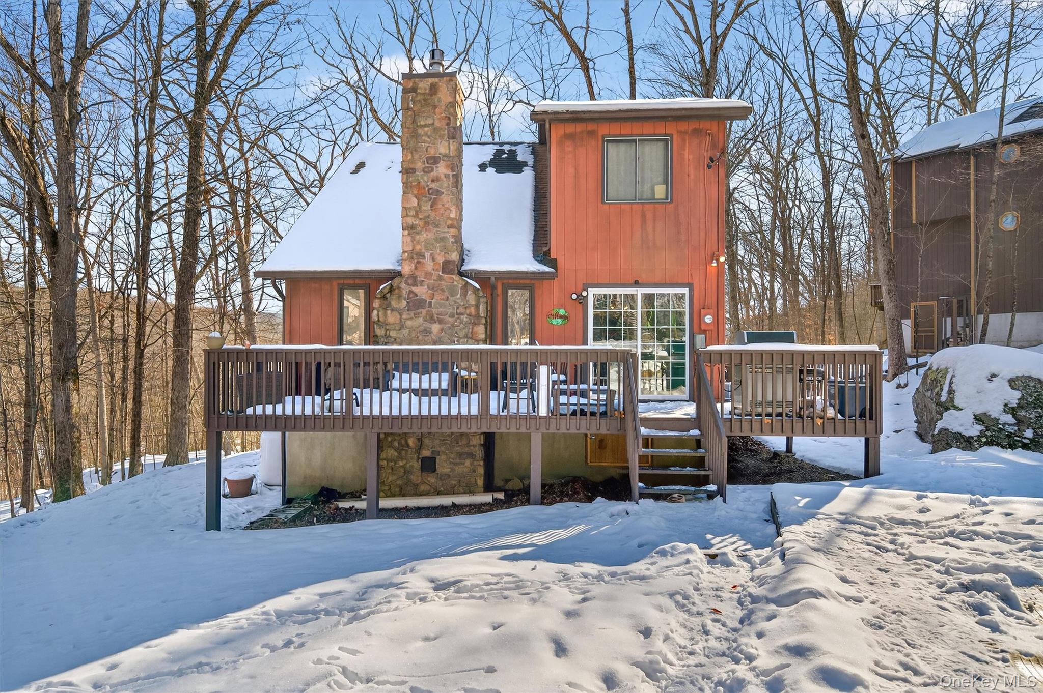 Snow covered house with a deck, stone siding, and a chimney