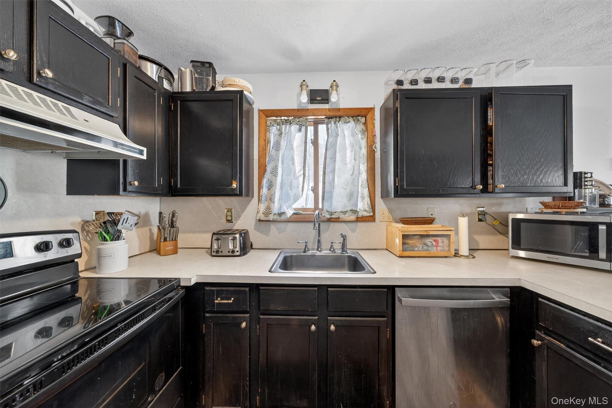 3111 Cherry Ridge Road Bushkill, PA 18324 - Photo 12 of 29 Kitchen with stainless steel appliances, light countertops, under cabinet range hood, a textured ceiling, and dark cabinets