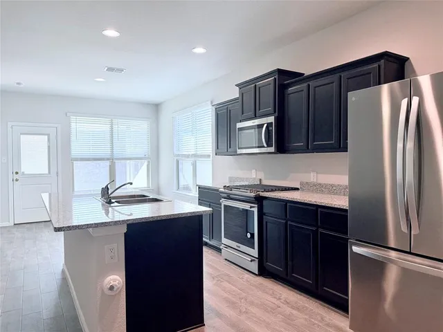 a kitchen with stainless steel appliances granite countertop a refrigerator a sink a stove and wooden cabinets