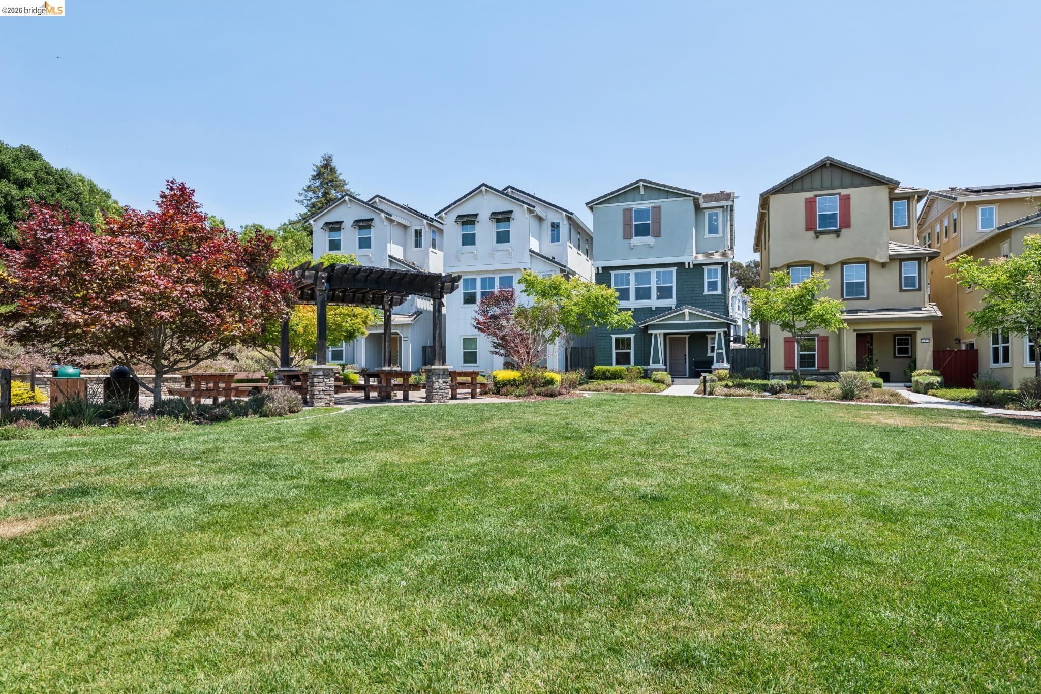 24157 Amaranth Loop Hayward, CA 94541 - Photo 62 of 63 Expansive community green space featuring a large lawn area, a dark wood pergola, stone-clad pillars, multiple picnic tables, and mature landscaping