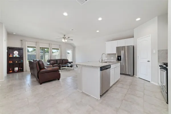 a large white kitchen with a refrigerator a stove top oven and couches