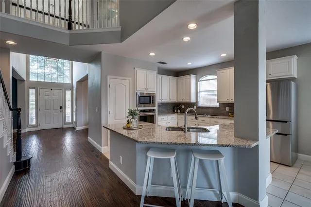 a kitchen with stainless steel appliances granite countertop a refrigerator a sink dishwasher a stove and a microwave oven with wooden floor