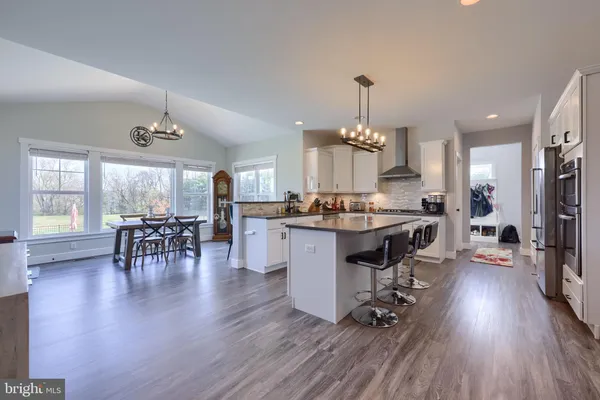 a open kitchen with stainless steel appliances granite countertop a stove top oven a sink dishwasher a dining table and chairs with wooden floor