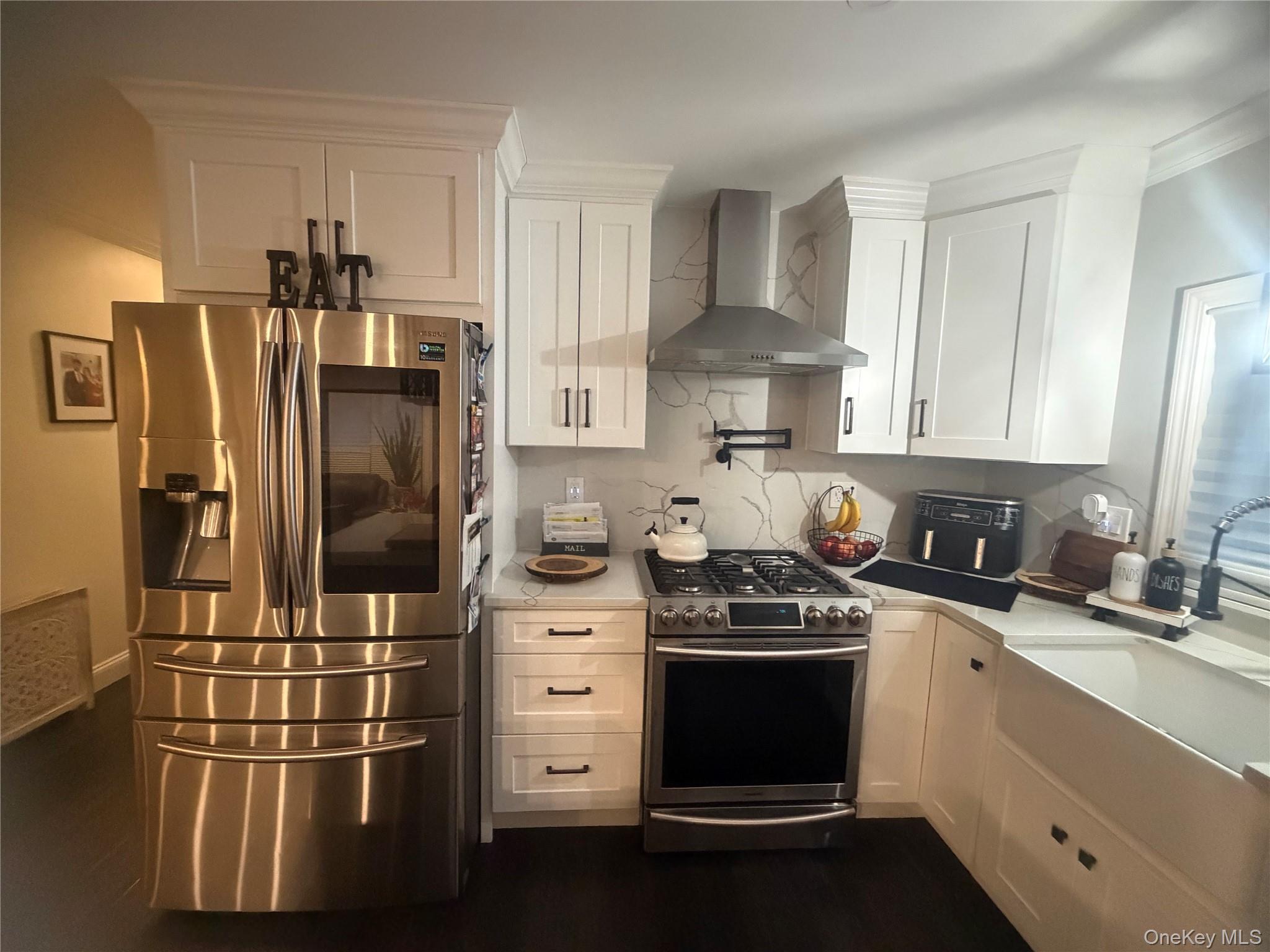 1580 North Jerusalem Road Merrick, NY 11566 - Photo 11 of 36 The kitchen features white cabinetry, dark flooring, and stainless steel appliances including a refrigerator and range with a matching range hood