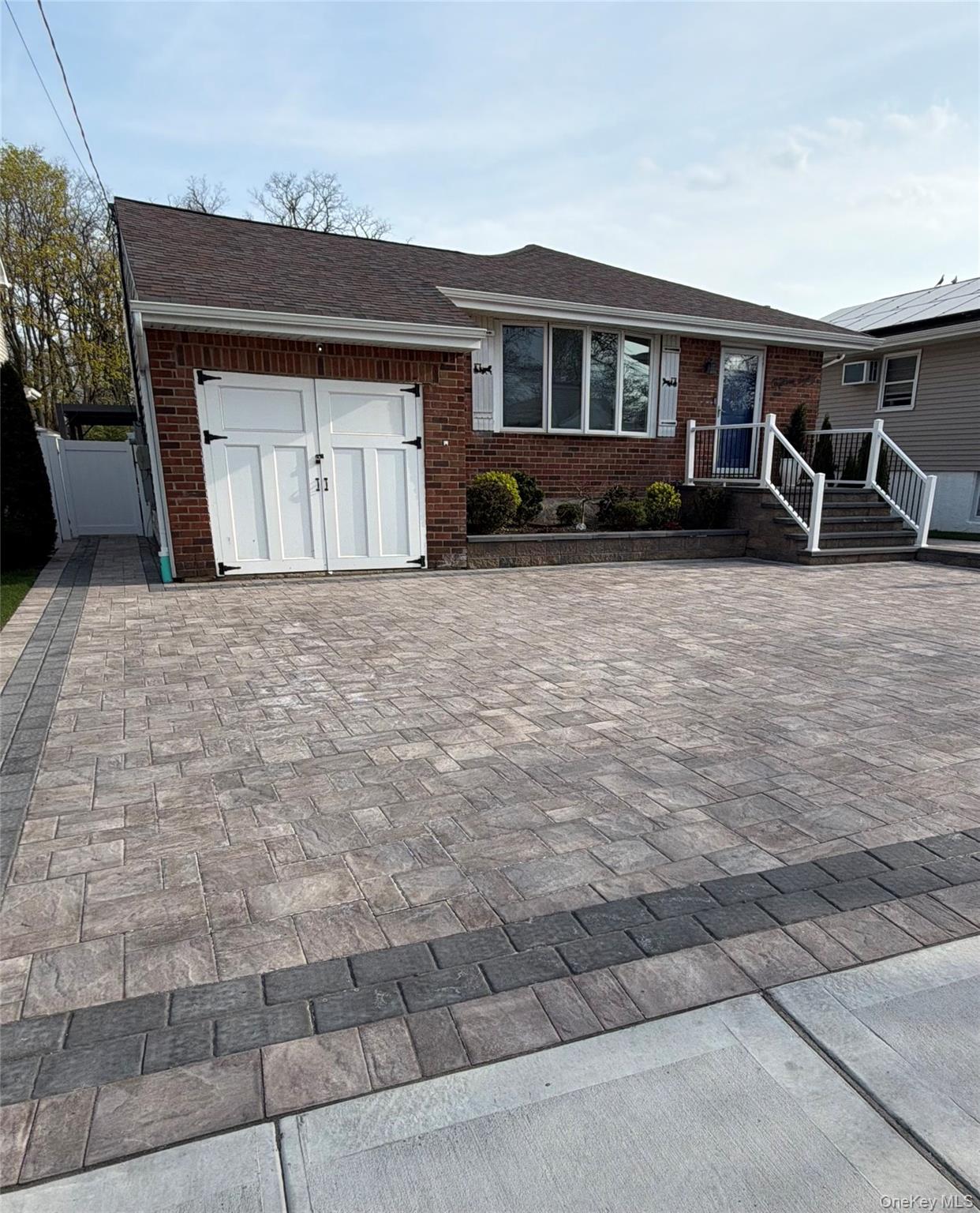 1580 North Jerusalem Road Merrick, NY 11566 - Photo 36 of 36 The property features an extensive paved driveway with an ornamental brick facade, a front door with white railings and steps, and an attached garage with white double doors