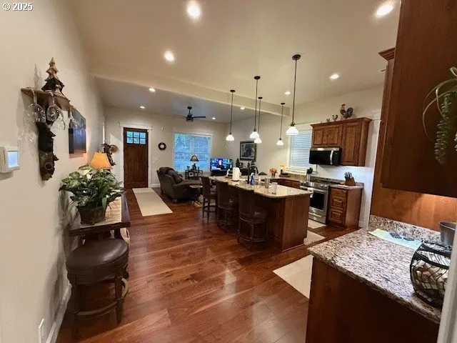 a kitchen with stainless steel appliances kitchen island granite countertop a refrigerator oven a sink a dining table and chairs with wooden floor