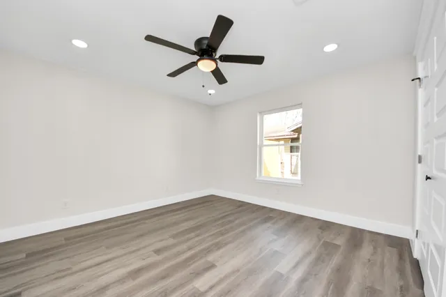 an empty room with wooden floor ceiling fan and windows