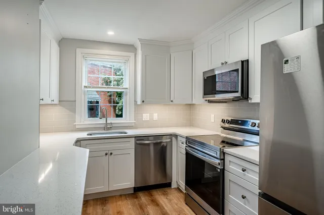 a kitchen with stainless steel appliances granite countertop white cabinets a sink a stove a microwave and wooden floors