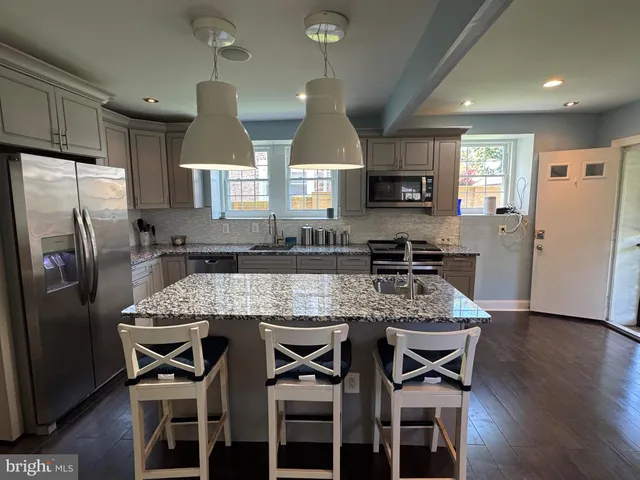 a kitchen with stainless steel appliances granite countertop a stove top oven a refrigerator a sink and chairs