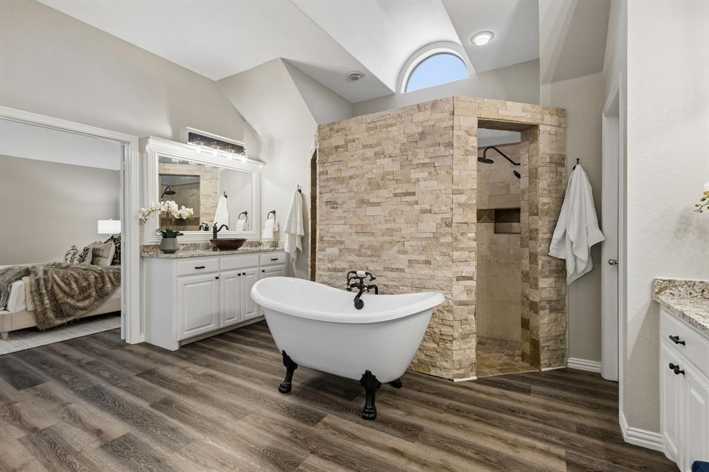 317 Singing Quail Trail Haslet, TX 76052 - Photo 16 of 32 Spacious bathroom featuring a freestanding clawfoot tub, a stone-tiled walk-in shower with an arched window, and dual vanities with granite countertops and undermount sinks