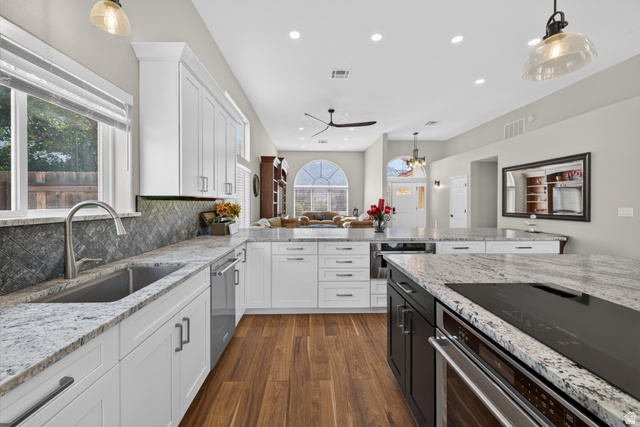 4297 Beeman Road Moab, UT 84532 - Photo 11 of 59 Modern kitchen featuring white cabinetry, light granite countertops, stainless steel appliances, wood-finish flooring, and a dark herringbone pattern backsplash