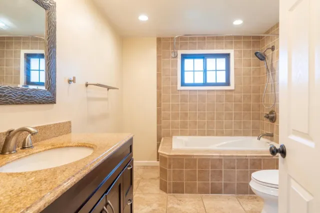 a bathroom with a granite countertop sink a toilet a mirror a bathtub and shower