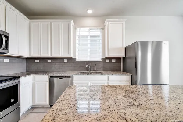 a large kitchen with granite countertop a refrigerator a stove a sink and white cabinets