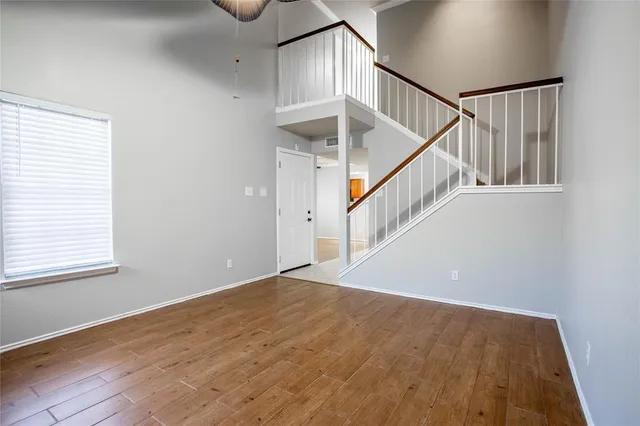 a view of an empty room with wooden floor and fan