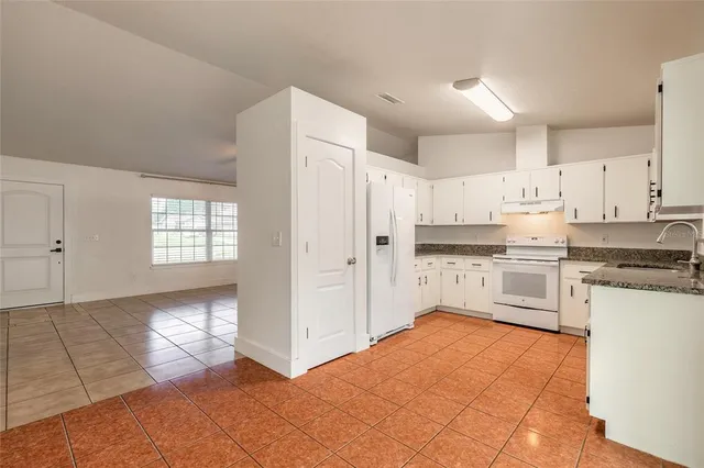 a large white kitchen with stainless steel appliances granite countertop a stove a sink and a refrigerator with white cabinets