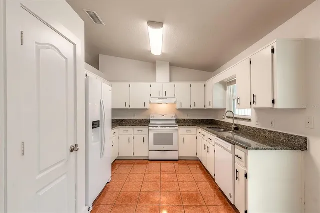 a kitchen with granite countertop a refrigerator stove top oven and sink
