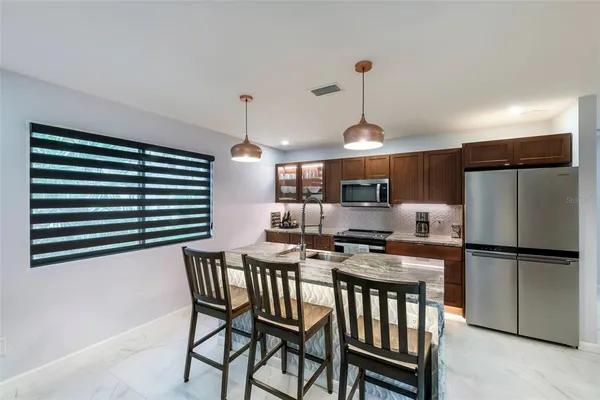 a kitchen with stainless steel appliances granite countertop a stove a refrigerator a kitchen island a dining table and chairs