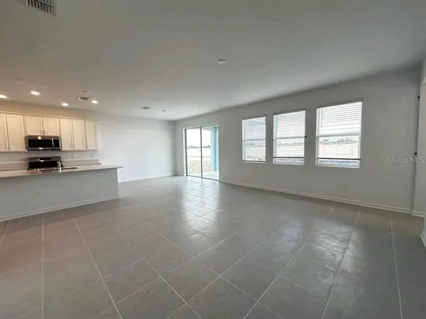 a view of an empty room with kitchen and window