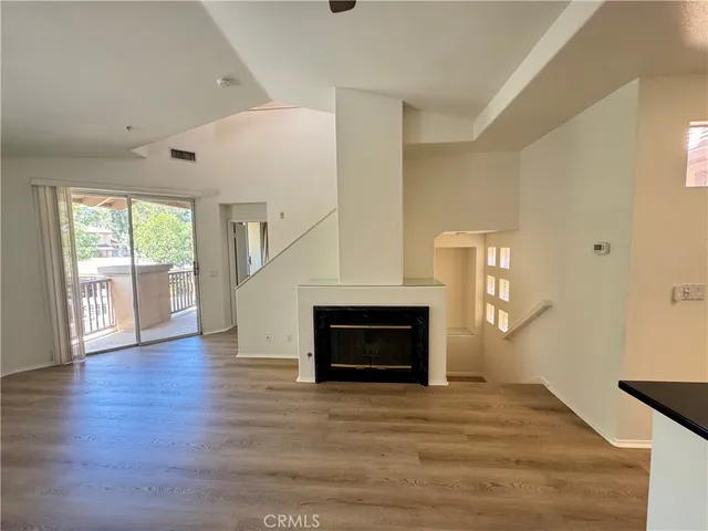 a view of an empty room with wooden floor fireplace and a window
