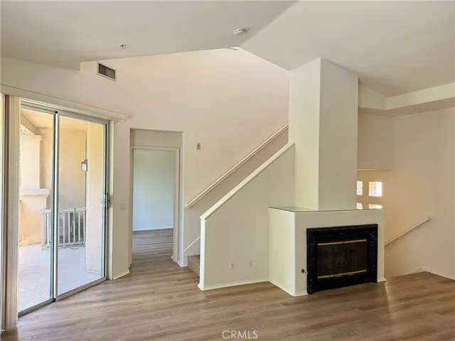 a view of an empty room with wooden floor fireplace and a window