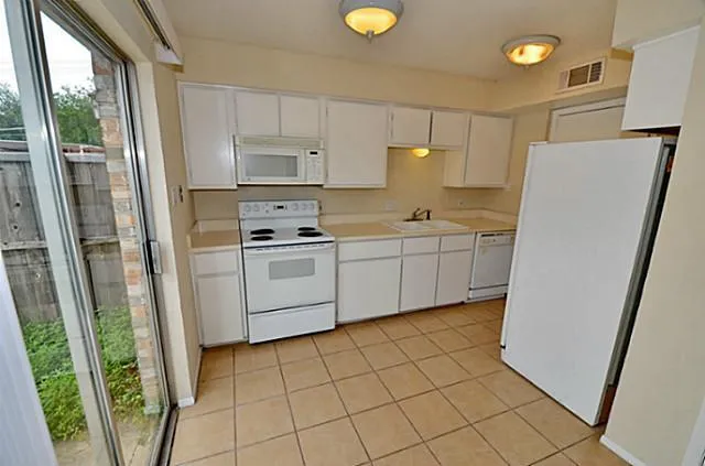 a kitchen with white cabinets a refrigerator a sink a stove a washer dryer and white cabinets