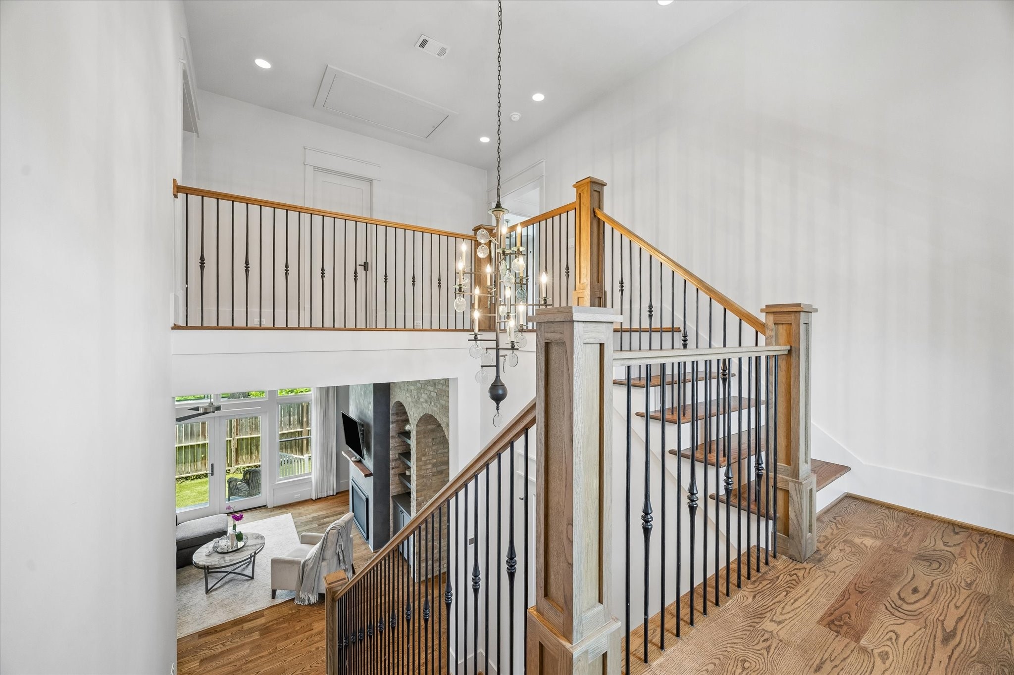 1101 Omar Street Houston, TX 77009 - Photo 24 of 46 This photo showcases a bright, airy stairwell with a modern chandelier, elegant wooden handrails, and iron spindles. The staircase overlooks a cozy living area with a fireplace, large windows, and hardwood floors, creating a welcoming and open space.
