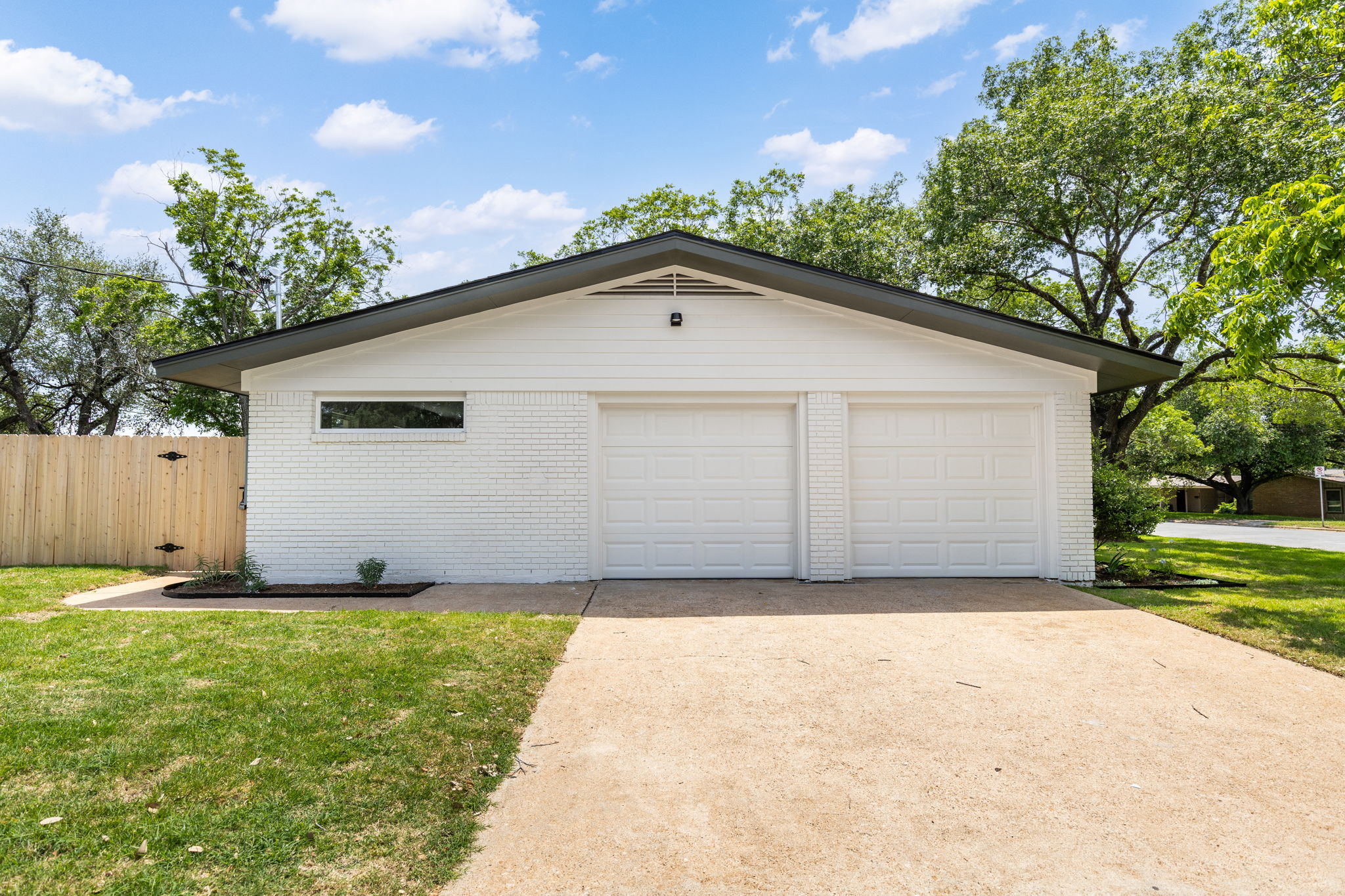 4501 Pack Saddle Pass Austin, TX 78745 - Photo 33 of 37 White brick exterior featuring a two-car garage with panel doors, a low-profile window, dark roofline, and a wooden fence with gate