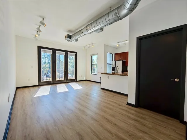 a view of an empty room with wooden floor and a kitchen