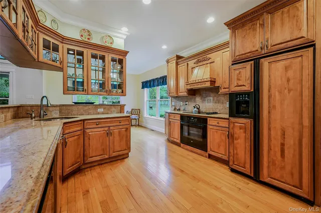 a kitchen with stainless steel appliances granite countertop wooden cabinets a refrigerator a sink a stove and a wooden floors