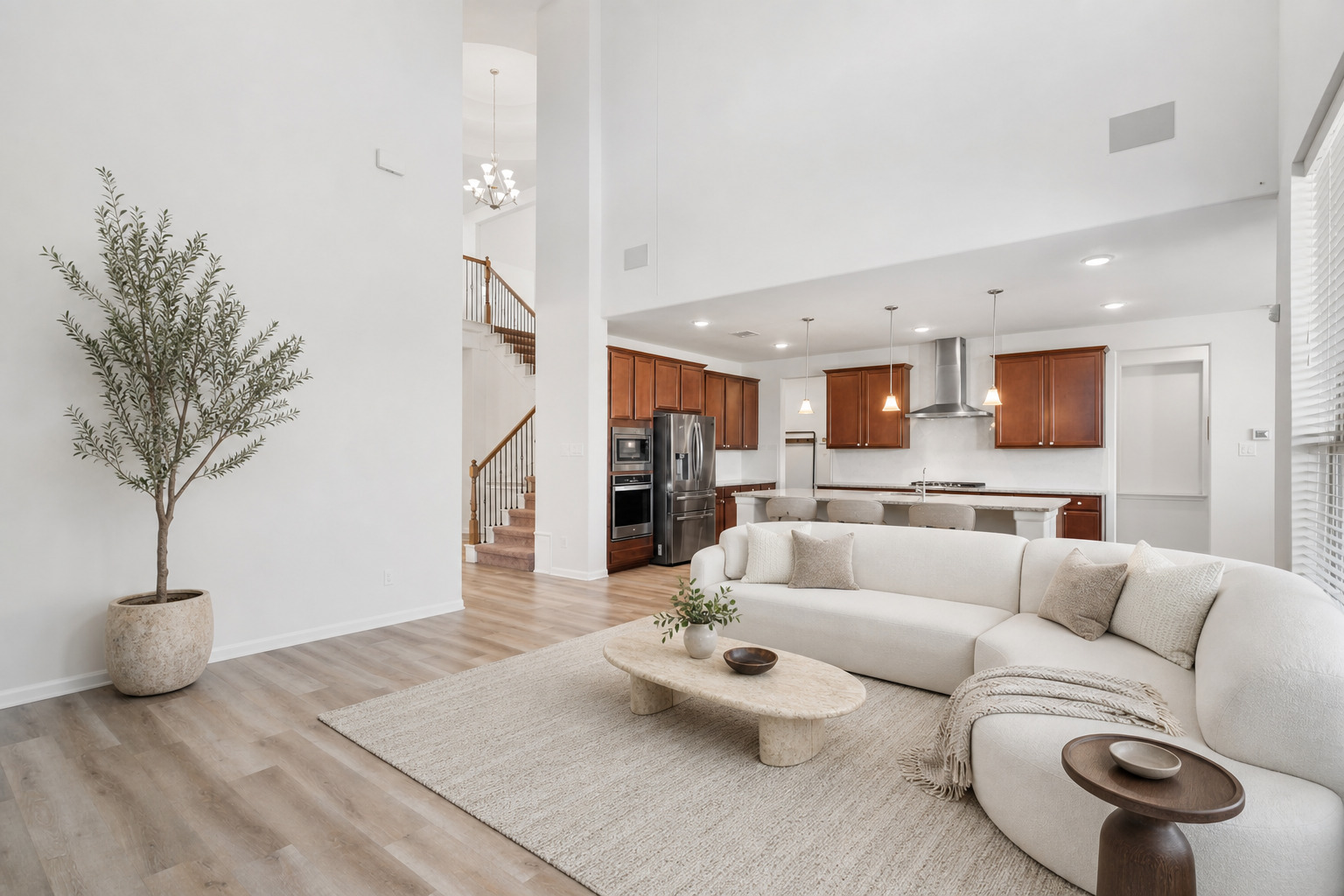 Double-height ceilings and tall windows illuminate a spacious living area flowing directly into the kitchen.
