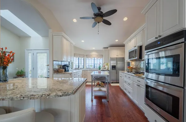 a kitchen with stainless steel appliances granite countertop a stove top oven a sink a dining table and chairs with wooden floor