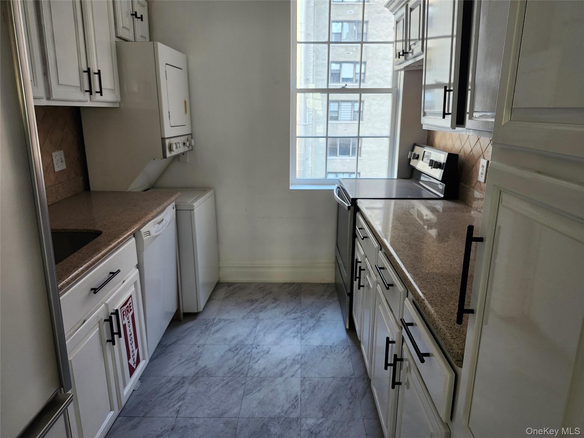231 East 62nd Street Manhattan, NY 10065 - Photo 17 of 17 Kitchen featuring tasteful backsplash, appliances with stainless steel finishes, stacked washing machine and dryer, and white cabinetry