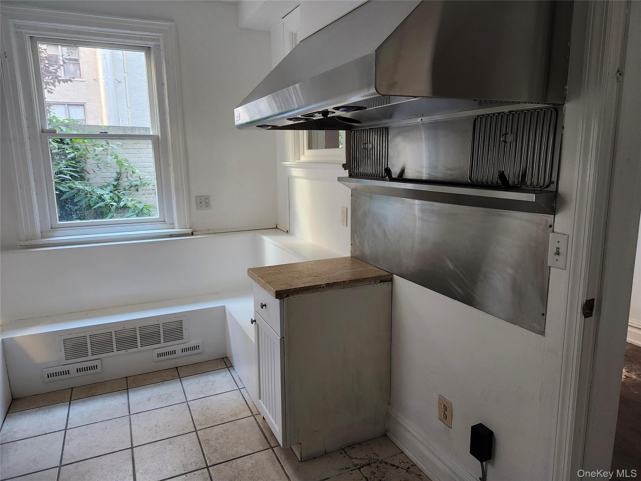 231 East 62nd Street Manhattan, NY 10065 - Photo 5 of 17 Kitchen with ventilation hood, white cabinetry, and light tile patterned floors
