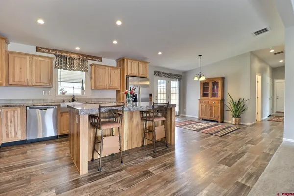 a kitchen with stainless steel appliances kitchen island granite countertop a refrigerator a stove a sink and a dining table with wooden floor