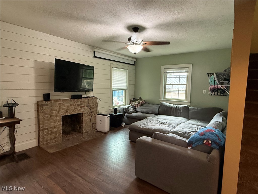 7350 Center Road Ashtabula, OH 44004 - Photo 5 of 20 Living room with dark wood-style flooring, ceiling fan, a textured ceiling, a brick fireplace, and wood walls